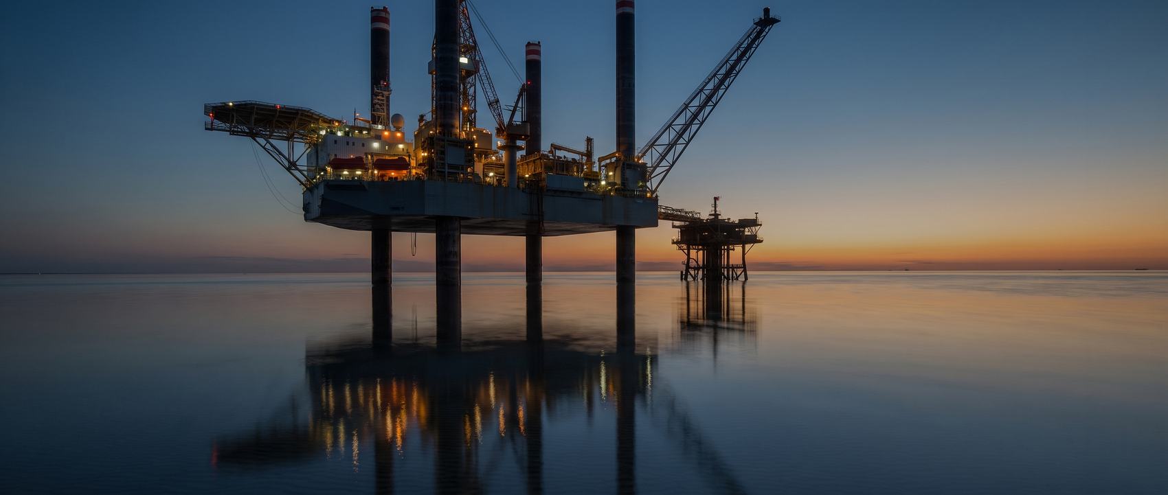 A jackup drilling rig standing on its legs in calm shallow sea at dusk